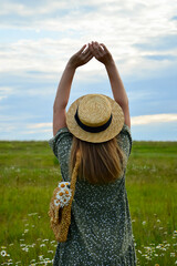 A young woman in a straw hat and with a straw bag on a chamomile field. Happy lady and nature - the concept of harmony. The idea of self-care, healthy lifestyle and positive