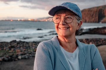 Portrait of happy senior woman outdoors at the beach enjoying sunset light looking at the horizon...