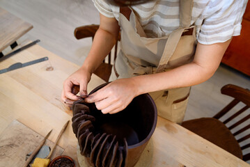 woman in pottery workshop working raw ceramic vase and clay to make pot. Pottery workshop with natural light scraping, smoothing, shaping and sculpting. making clay pot