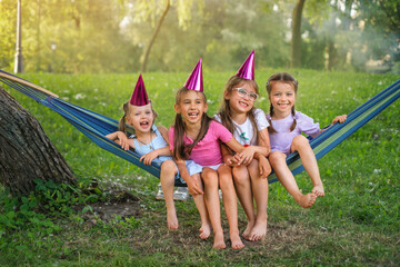 Four funny laughing girls swing together on a hammock in the park on the birthday of one of their friends.