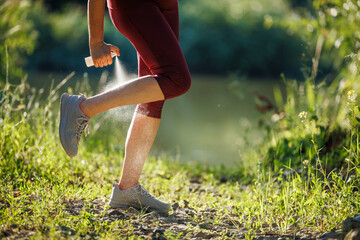 Woman applying insect repellent against mosquito and tick on her leg before jogging in nature - obrazy, fototapety, plakaty