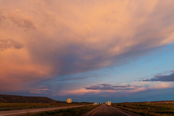 Naklejka na ściany i meble Scenic landscape with highway among mountains and colorful sky at dusk. Blue, orange and purple sky at sunset over the road. Highway 40, Arizona, USA - 06-17-2022