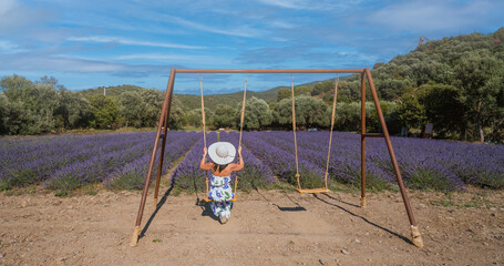 young woman with white straw hat plays with the swing in front of a lavender field