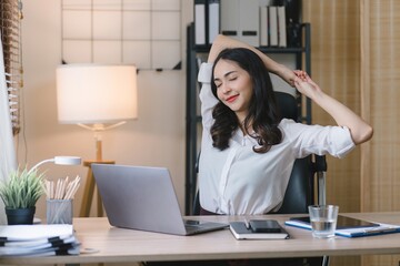A businesswoman stretches lazily on her desk for relaxation while working in the office.