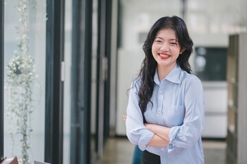 Happy young Asian businesswoman leader arm crossed, standing in an office. Professional executive manager or saleswoman using corporate technology, confidently looking at the camera.