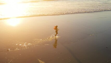 Aerial shot of a fit asian woman jogging on the beach at sunset