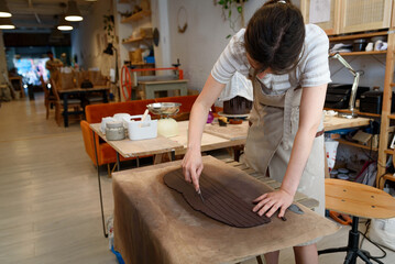 woman in pottery workshop working raw ceramic vase and clay to make pot. Pottery workshop with natural light scraping, smoothing, shaping and sculpting. making clay pot