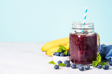 Blueberry banana smoothie in glass jar at blue background.