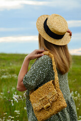 A young woman in a straw hat and with a straw bag on a chamomile field. Happy lady and nature - the concept of harmony. The idea of self-care, healthy lifestyle and positive