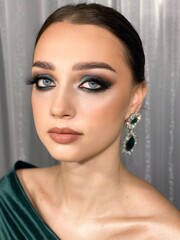 Portrait of a blue-eyed girl with luxurious smokey ice makeup and emerald earrings