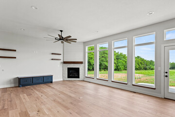 Large family room with window, fire place, white walls, sanded hardwood floors, and large window