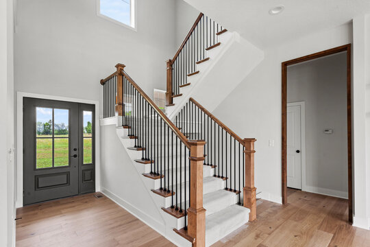 staircase in a house with stained wood rail, black spindles and end caps - white staircase, and carpeted, pattern runner. 