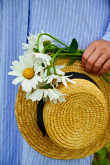 A young woman in a straw hat  on a chamomile field. Happy lady and nature - the concept of harmony. The idea of self-care, healthy lifestyle and positive