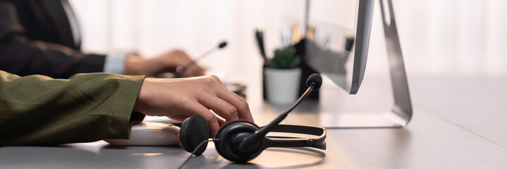 Panorama focus hand holding headset on call center workspace desk with blur background of operator...