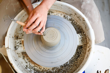 close up of ceramist hands working and shaping ceramic on the lathe or potter's wheel inside a pottery workshop with natural light