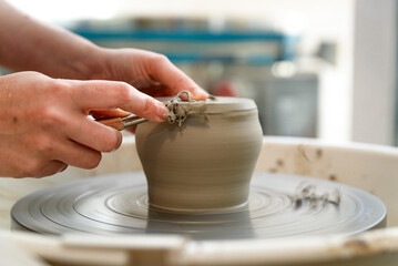 close up of raw ceramic running on the lathe or potter's wheel, with hands with tool refining fine details of vase