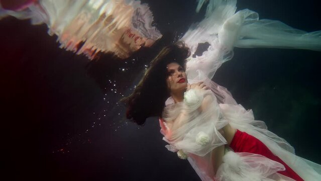 graceful woman swimming alone underwater, enigmatic lady floating under water surface, slow motion