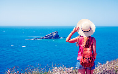 Rear view of woman with hat and backpack looking at atlantic ocean and island view- Brittany in France- travel destination, vacation,  adventure concept