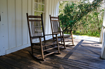 Fototapeta na wymiar Old vintage rocking chairs sitting on a colonial style Florida house porch with trees in background