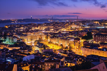 Fototapeta na wymiar Night view of Lisbon famous view from Miradouro da Senhora do Monte tourist viewpoint of Alfama and Mauraria old city districts, 25th of April Bridge in the evening twilight. Lisbon, Portugal