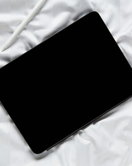 Flat lay top view blank screen digital tablet on white bed. Home office workspace