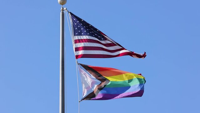 The US flag and the Progress Pride Flag blowing in the wind. Slow Motion.