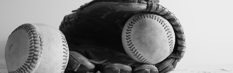 Retro style black and white still life banner scene of used baseballs with ball glove background. © ccestep8