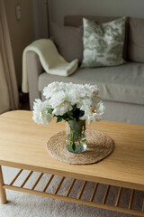 Home cozy interior. Bouquet of peonies in a glass vase on a wooden coffee table. Spring.