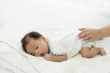 Fototapeta na wymiar Newborn baby sleeping in prone position on bed. Newborn baby or infant lying on white bed while mother’s hands takes care carefully. Family, love and new life concept