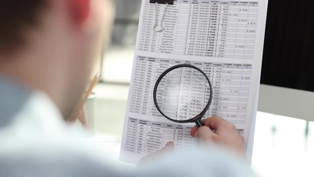 man looking through a magnifying glass to documents notebook.