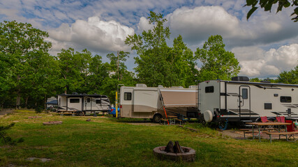 Rv motorhome and trailers backed into campsite cloudy sky fire pit and picnic tables on grass 