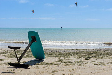 A kitesurf board resting alone on the sand of the beach with two kitesurfers surfing in the...