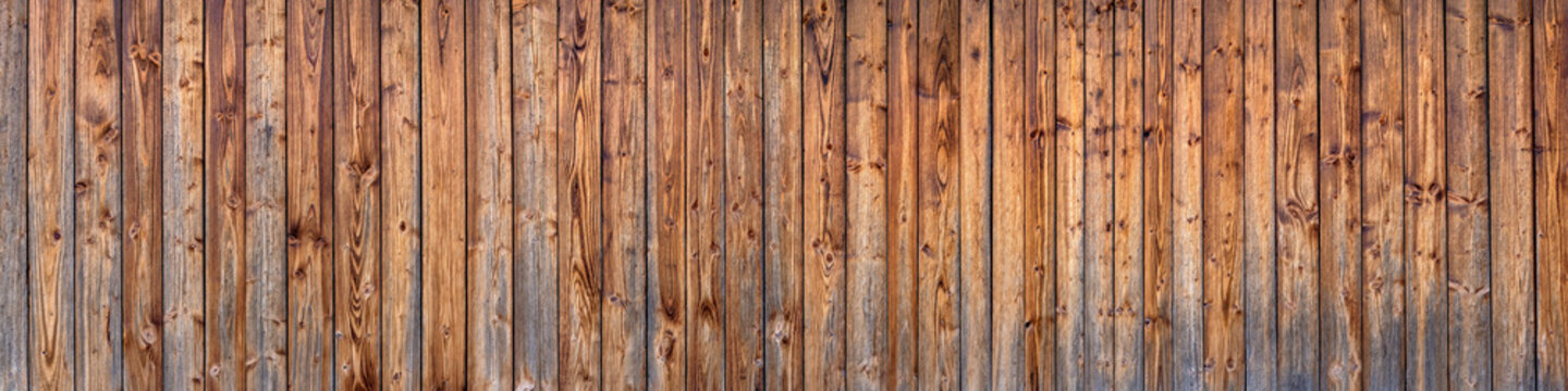 Panorama Holzwand einer Scheune aus braunen vertikalen, bereits verwitterten Brettern mit intensiver Maserung