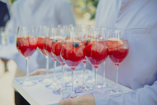 glasses of chamA tray of elegant red cocktails garnished with fresh berries, served at an event by waitstaff in white attire.pagne