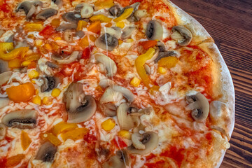 Funghi pizza with tomato sauce, cheese, mushrooms, peppers and corn on wooden table