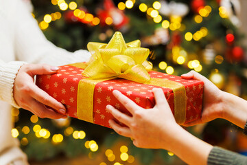 Hands of parent giving Christmas gift to child on Christmas tree background