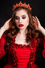 Portrait of a young, attractive vampire woman in a red dress in the rococo era with a crown on her head, posing isolated on a dark background.