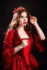 Portrait of a young, attractive vampire woman in a red dress in the rococo era with a crown on her head, posing isolated on a dark background.