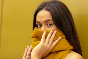 Latin woman covers her face with a scarf and she's looking at the camera to the side. Fashionable.