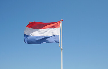 Flag of the Netherlands waving in the wind against a clear blue sky