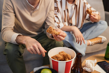Closeup young couple eating fried chicken takeout while watching TV at home, copy space