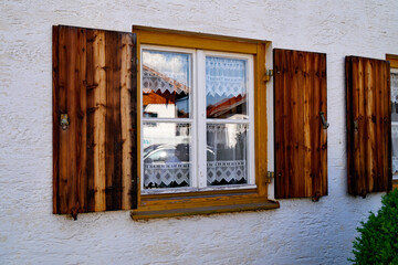 a traditional Bavarian rustic window with cute white lacy drapes and wooden shutters in the Bavarian Alps in Schwangau in the Bavarian Alps, Bavaria, Germany	