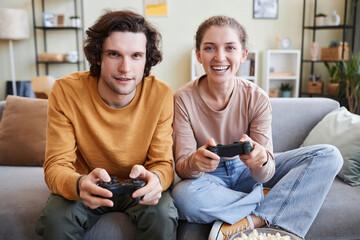 Front view at smiling young couple playing video games together and holding controllers