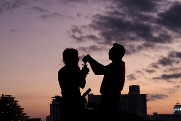 Fototapeta na wymiar Sunset silhouette of two men lighting a smoke against a beautiful purple sky