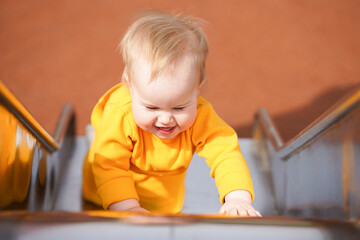 Cheerful baby toddler plays on the playground in the summer