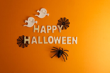 Happy Halloween lettering on orange background with halloween decor spider, cobweb and ghost 