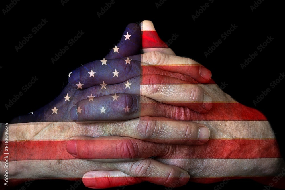 Wall mural closeup of man's praying hands with american flag overlay isolated on black background