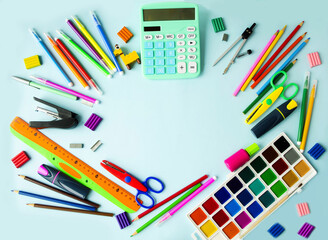 School supplies lie in a circle on the table on a blue background, pens, paints, pencils, scissors,...