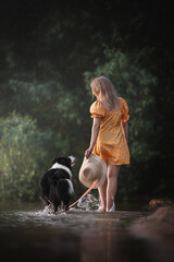 Girl in yellow dress walking in water with a border collie dog