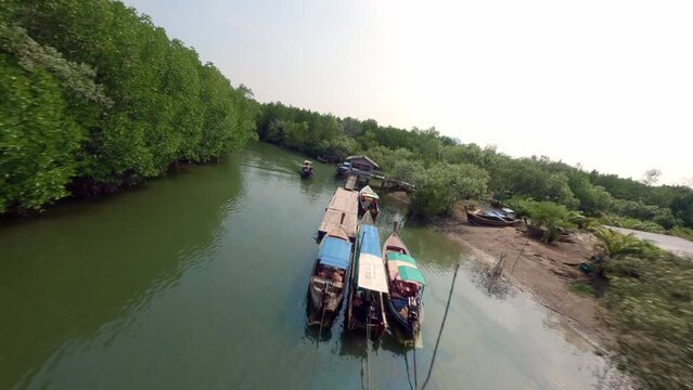 Touristic Asian longtail boat mooring approaching fishing village embankment authentic harbor port aerial view. FPV sport drone shot traditional tropical countryside pier water transport river forest